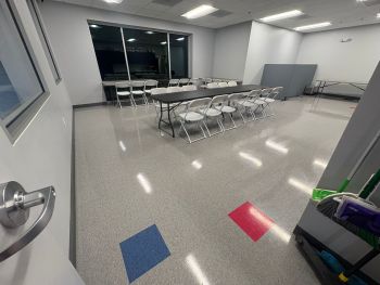 Empty classroom with folding tables and chairs, open door, and polished floor under ceiling lights